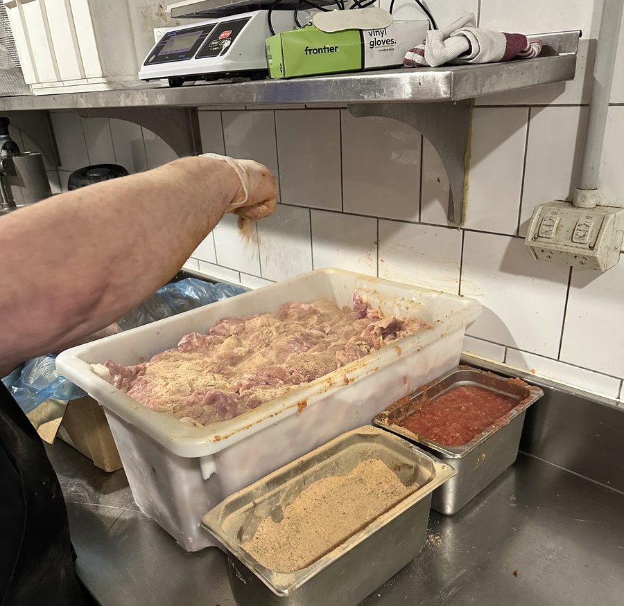 Housemade dry spice and Greek herb blend being sprinkled over raw chicken maryland at Yassas restaurant kitchen - charcoal gyros preparation Melbourne